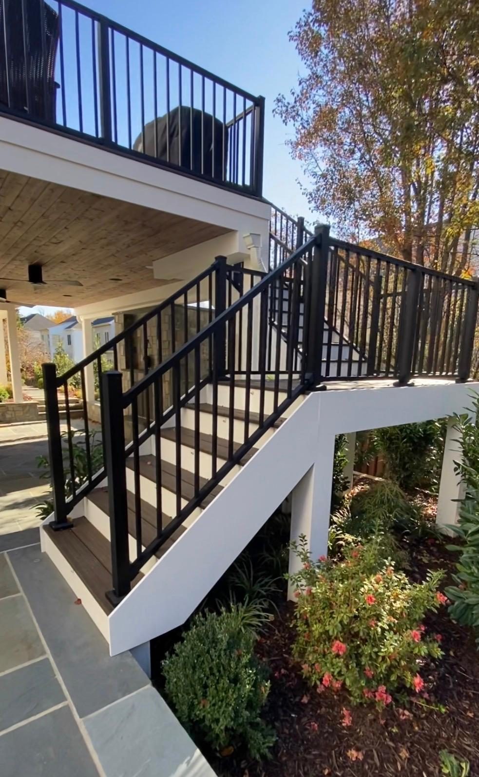 Composite stairs with black aluminum railing and an intermediate landing, running down from an elevated deck to a flagstone patio
